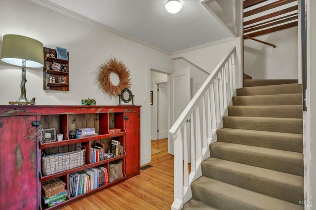 staircase with wood finished floors, crown molding, and visible vents
