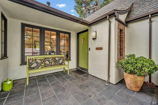 view of exterior entry with stucco siding and roof with shingles
