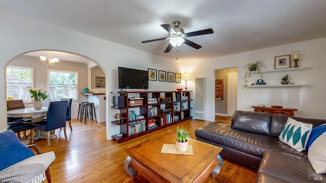 living room featuring arched walkways, ceiling fan with notable chandelier, a textured ceiling, and wood finished floors