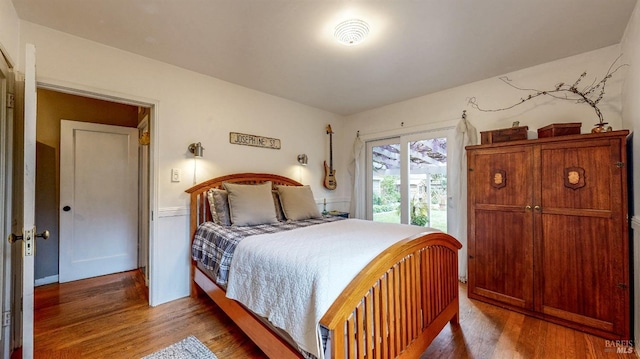 bedroom with access to outside, wainscoting, and wood finished floors