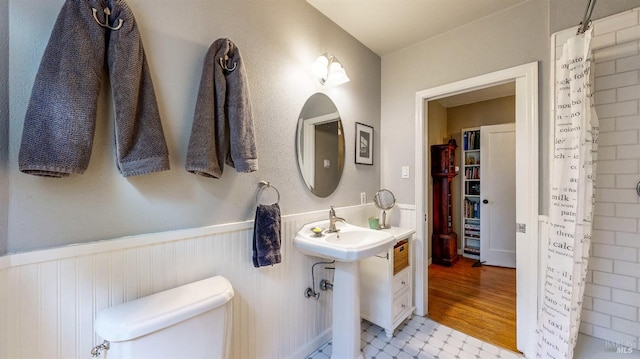 full bath with toilet, a wainscoted wall, a shower with shower curtain, and a sink