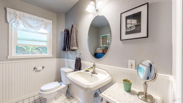 half bath with toilet, a wainscoted wall, a sink, and tile patterned floors