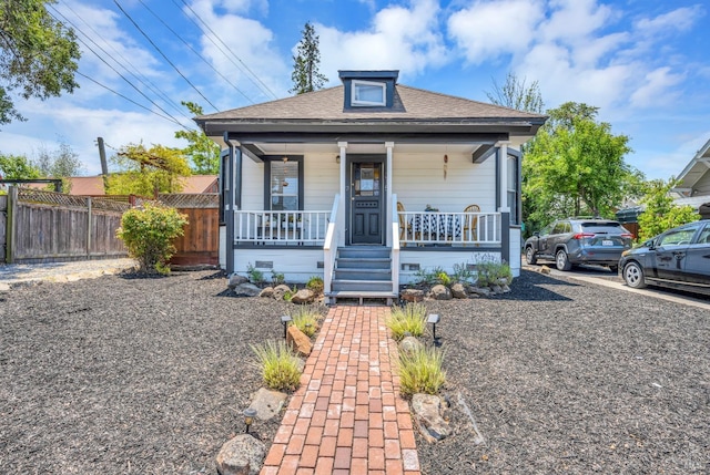 bungalow featuring covered porch, fence, and a shingled roof
