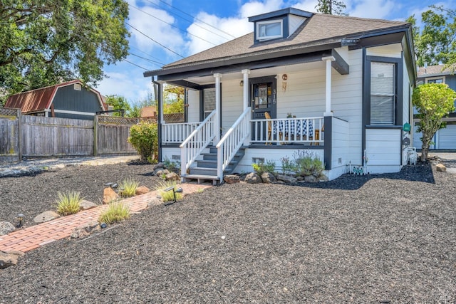 bungalow with a porch, roof with shingles, and fence