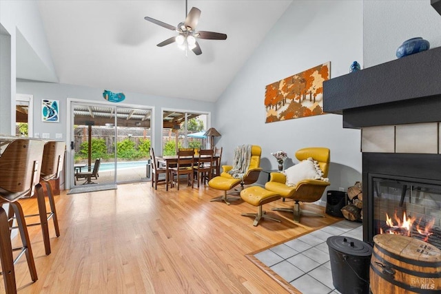 interior space featuring a glass covered fireplace, high vaulted ceiling, a ceiling fan, and wood finished floors