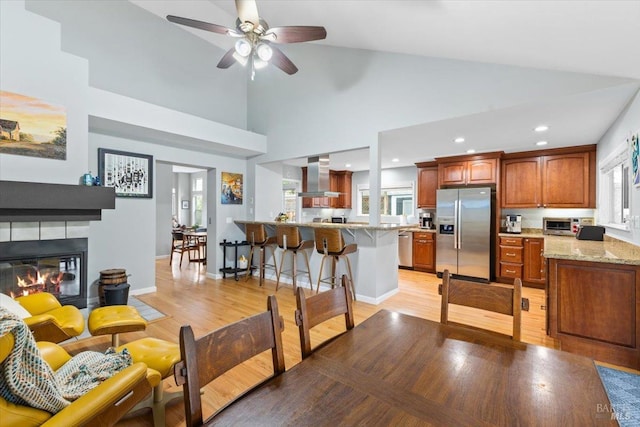 living room featuring light wood-style floors, a glass covered fireplace, ceiling fan, and high vaulted ceiling