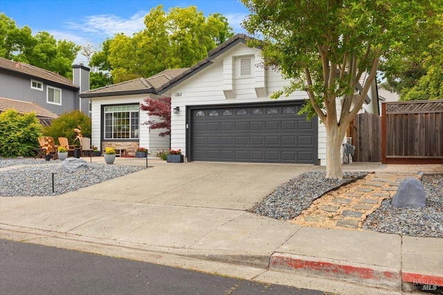 traditional-style house featuring fence, a tiled roof, concrete driveway, and a garage