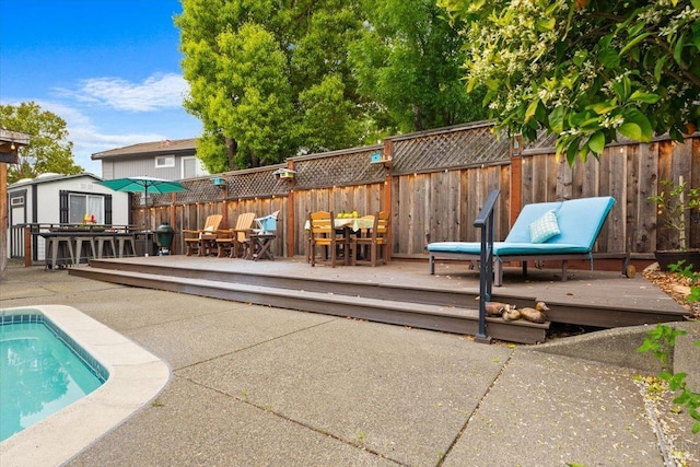 view of pool featuring an outdoor structure, fence, a wooden deck, and outdoor dining space