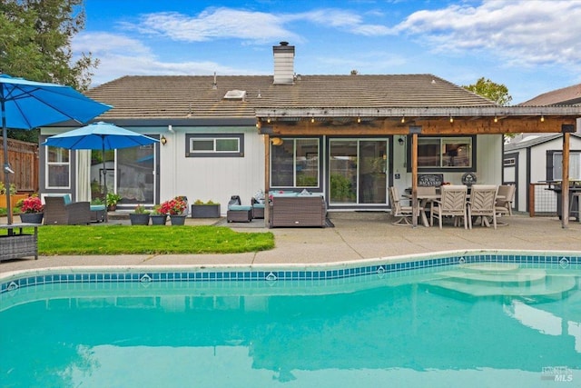rear view of house with an outdoor living space, an outdoor pool, a chimney, and a patio
