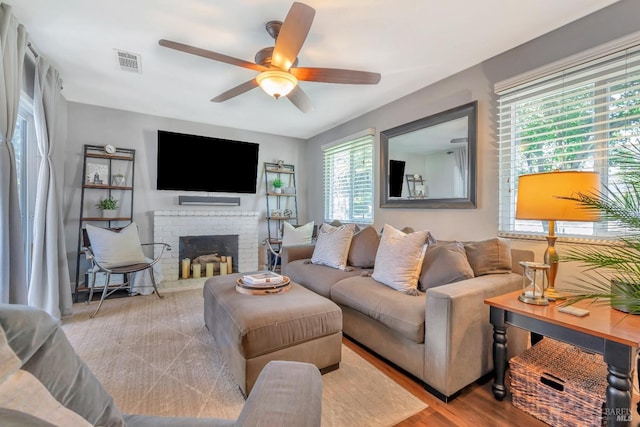 living area with visible vents, wood finished floors, a ceiling fan, and a fireplace
