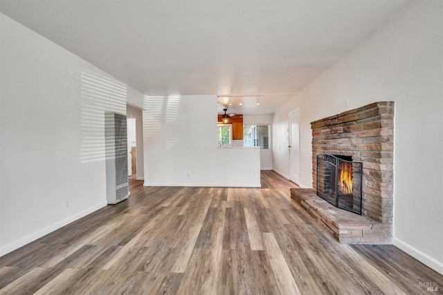 unfurnished living room with baseboards, track lighting, wood finished floors, and a fireplace