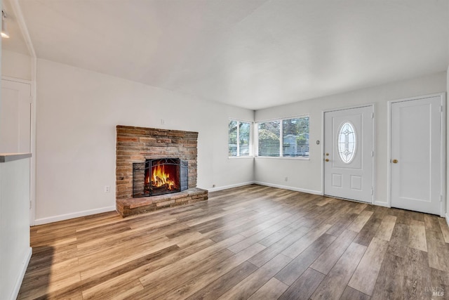 unfurnished living room with baseboards, a lit fireplace, and wood finished floors
