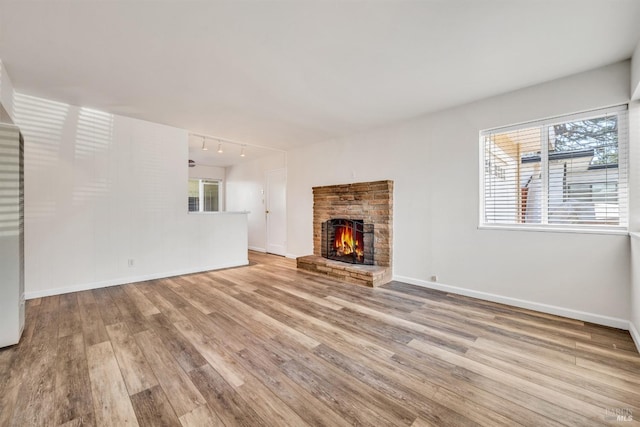 unfurnished living room with baseboards, rail lighting, a brick fireplace, and wood finished floors