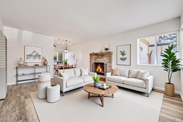 living room featuring rail lighting, a stone fireplace, baseboards, and light wood-type flooring
