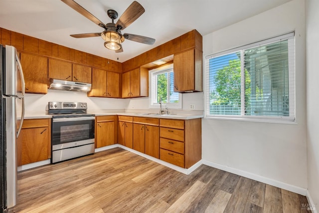 kitchen featuring light countertops, under cabinet range hood, a sink, light wood finished floors, and stainless steel appliances