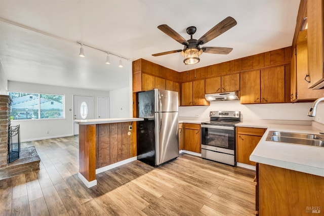 kitchen with brown cabinetry, appliances with stainless steel finishes, rail lighting, a sink, and light countertops