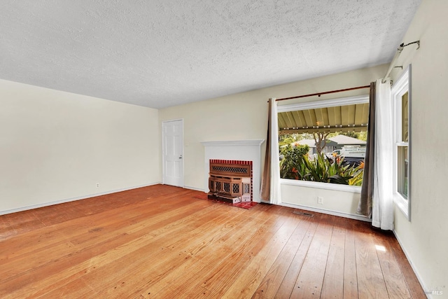 unfurnished living room with a textured ceiling, visible vents, hardwood / wood-style flooring, and baseboards