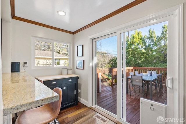 doorway featuring baseboards, ornamental molding, wood finished floors, and visible vents