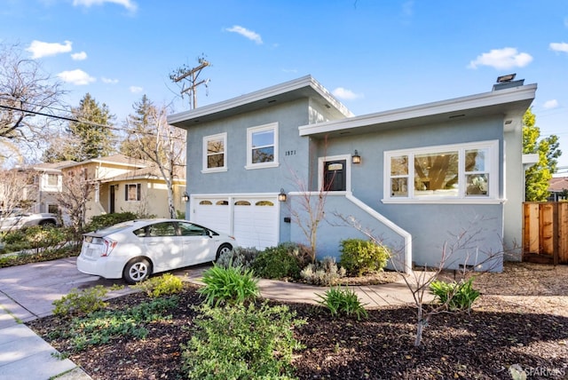 tri-level home with fence, stucco siding, a chimney, an attached garage, and driveway