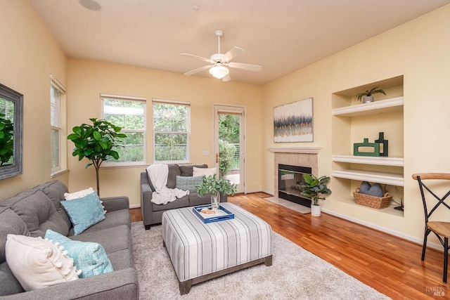 living area with built in features, a ceiling fan, baseboards, wood finished floors, and a tile fireplace