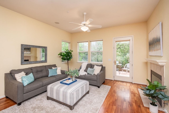 living area featuring a fireplace, ceiling fan, baseboards, and light wood-style floors