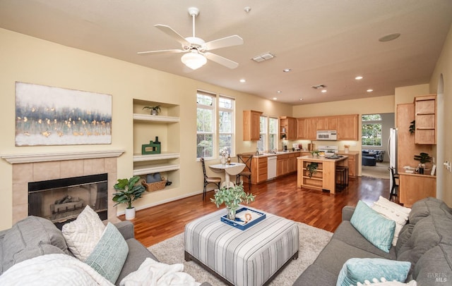 living room featuring a fireplace, dark wood finished floors, built in features, a ceiling fan, and visible vents