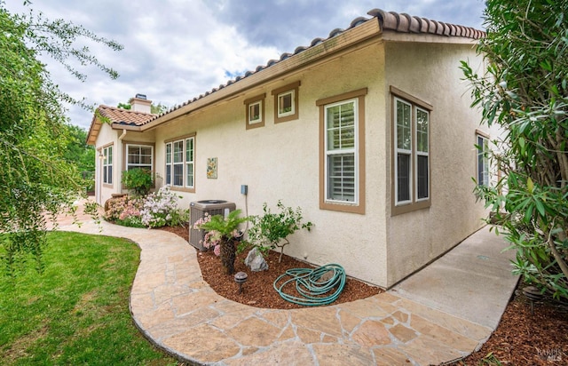 exterior space with central AC unit, stucco siding, and a tile roof