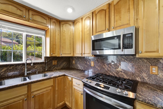 kitchen with dark stone counters, appliances with stainless steel finishes, decorative backsplash, and a sink