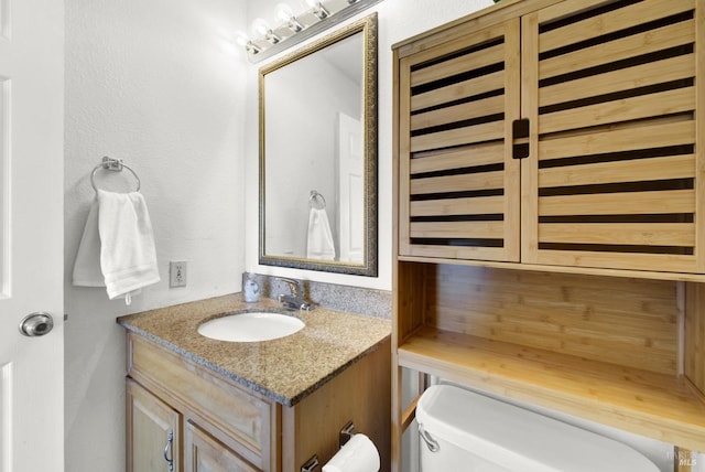 bathroom featuring toilet, a textured wall, and vanity