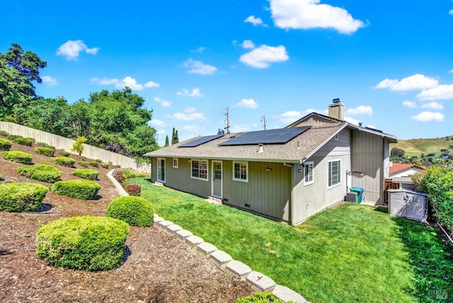 back of property featuring a fenced backyard, a chimney, a shingled roof, roof mounted solar panels, and a yard