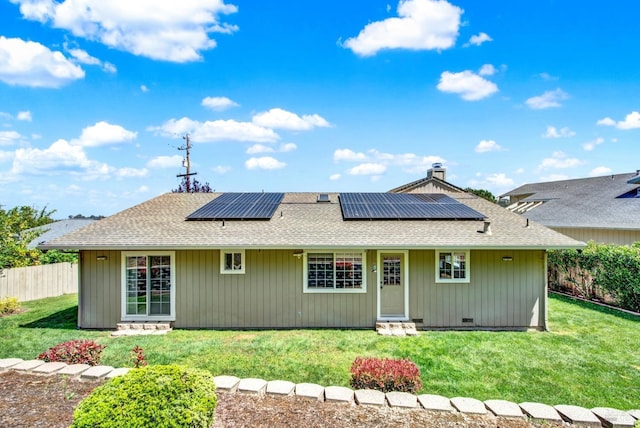 back of house with a yard, fence, solar panels, and roof with shingles