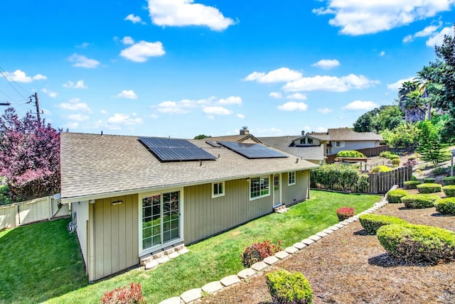 rear view of house with roof with shingles, a fenced backyard, a yard, and roof mounted solar panels
