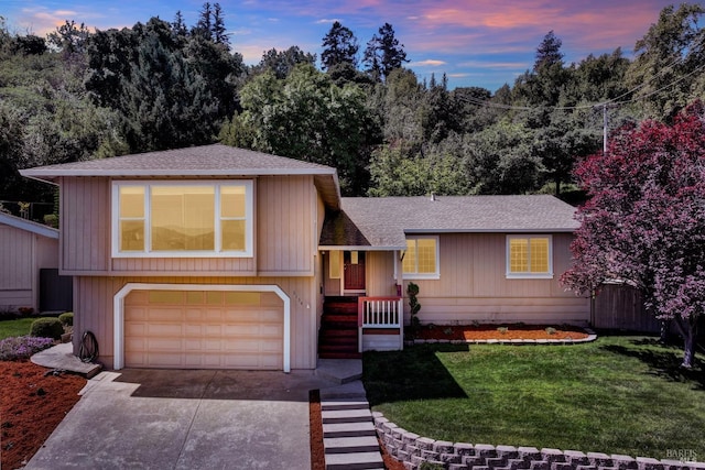 tri-level home with an attached garage, driveway, a shingled roof, and a front yard