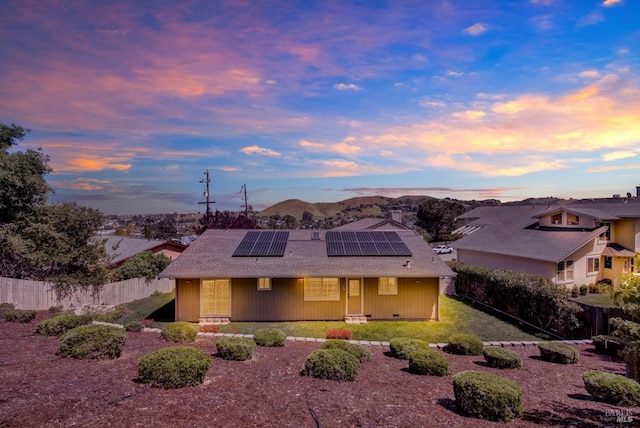 view of front facade with fence, a shingled roof, roof mounted solar panels, a porch, and a mountain view