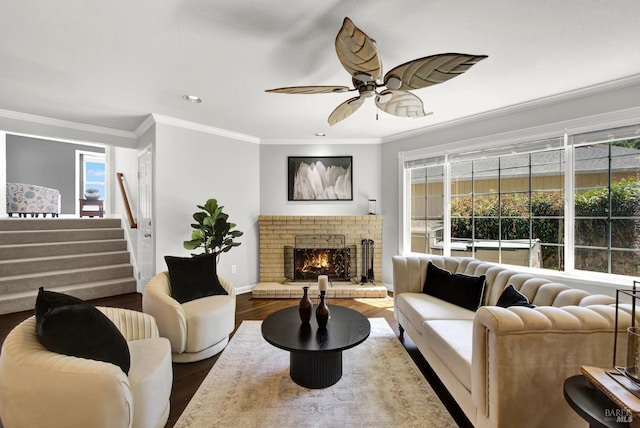 living area with crown molding, stairs, wood finished floors, a fireplace, and ceiling fan