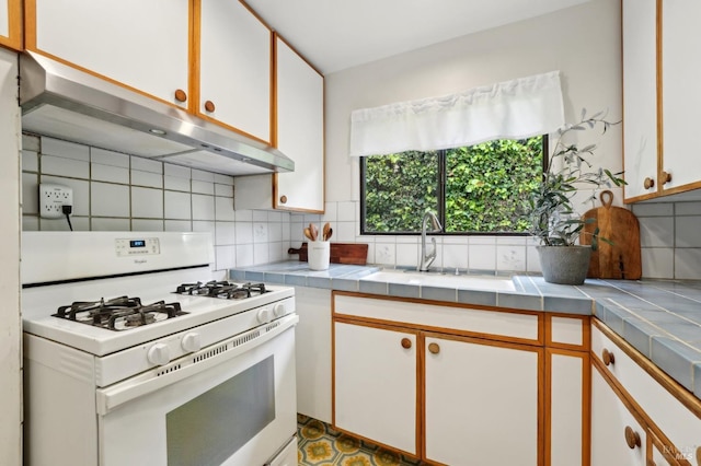 kitchen with white range with gas stovetop, tile countertops, under cabinet range hood, and decorative backsplash