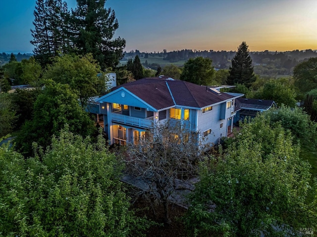 back of property at dusk featuring a balcony and roof with shingles