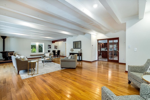 living room featuring light wood-style floors, a wood stove, beamed ceiling, and baseboards