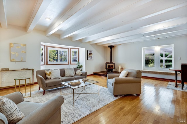 living room with light wood-type flooring, beamed ceiling, a wood stove, and baseboards