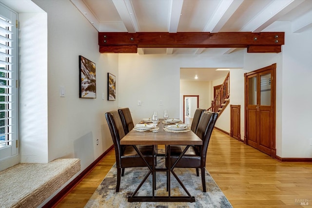 dining space featuring beamed ceiling, light wood finished floors, and plenty of natural light