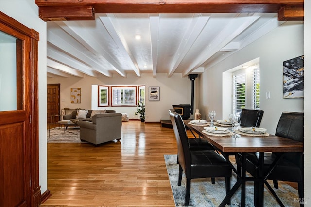 dining area with light wood-type flooring, beamed ceiling, and a wood stove