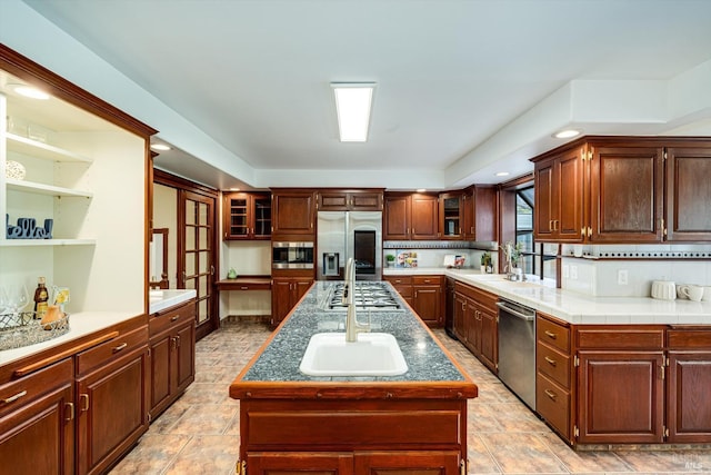 kitchen with open shelves, glass insert cabinets, a sink, stainless steel appliances, and a kitchen island with sink
