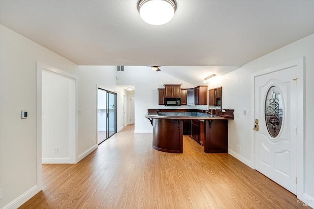 kitchen featuring light wood finished floors, a kitchen bar, black microwave, visible vents, and lofted ceiling