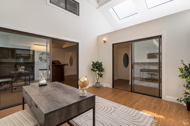 living room with baseboards, high vaulted ceiling, a skylight, and wood finished floors