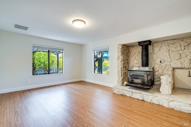 unfurnished living room with baseboards, visible vents, wood finished floors, and a wood stove