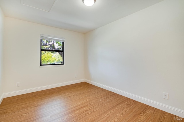 unfurnished room with attic access, light wood-type flooring, and baseboards