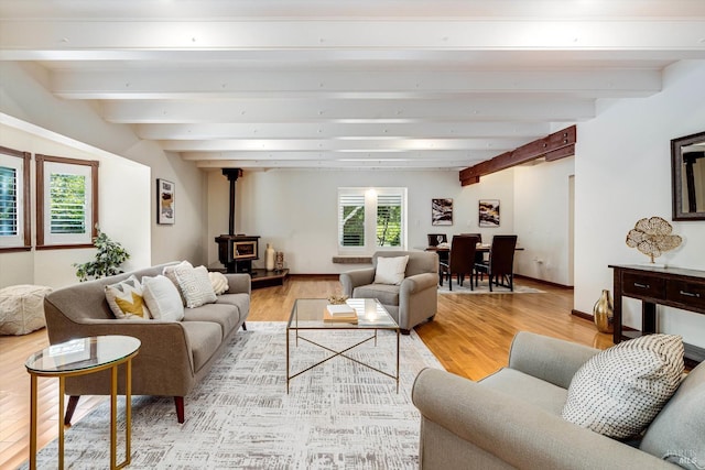 living area with light wood-type flooring, beamed ceiling, a wood stove, and baseboards