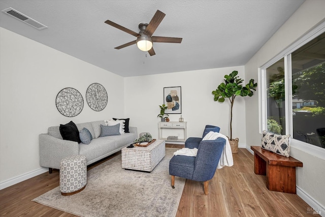 living area featuring baseboards, ceiling fan, wood finished floors, and visible vents