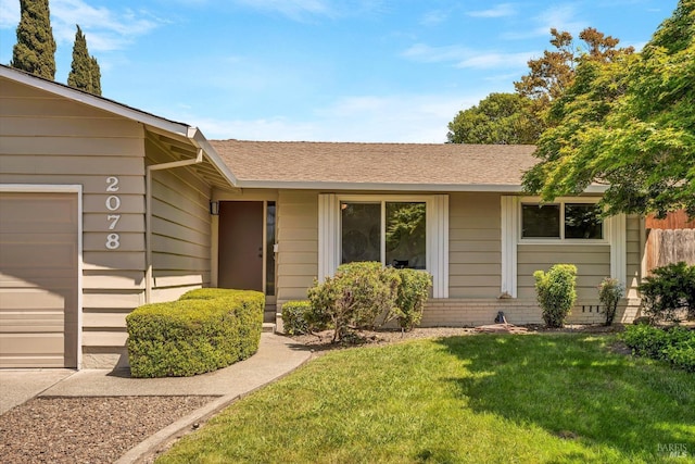 view of exterior entry featuring a lawn, a garage, and a shingled roof