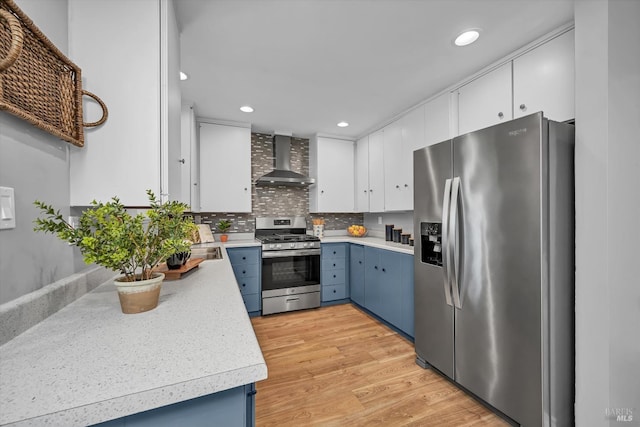 kitchen featuring light countertops, appliances with stainless steel finishes, wall chimney exhaust hood, and blue cabinets